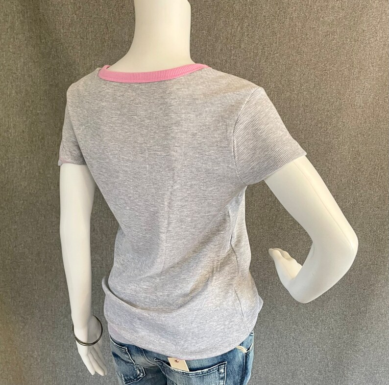 May include: Gray short-sleeved t-shirt with a pink ribbed trim around the neckline.