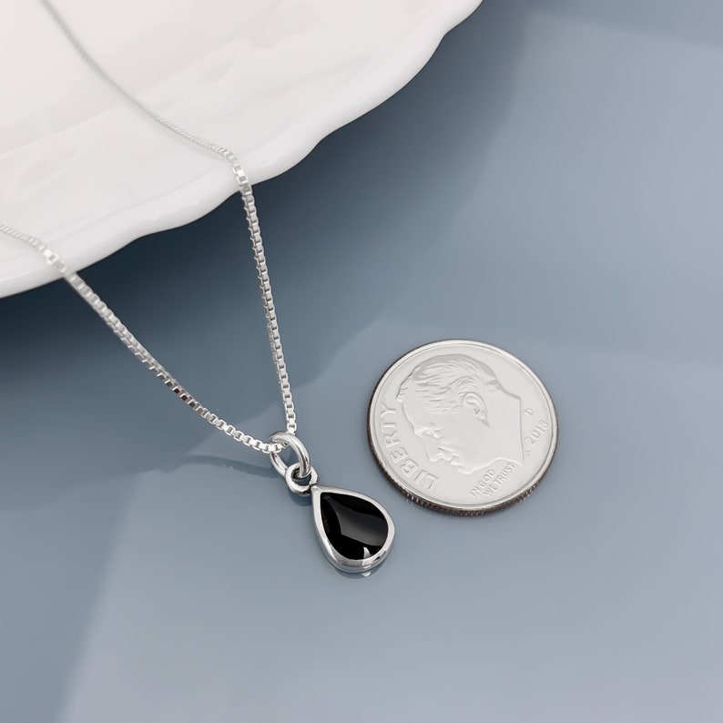 May include: A silver chain necklace with a teardrop-shaped pendant featuring a black gemstone. The pendant is about the size of a ten pence piece.