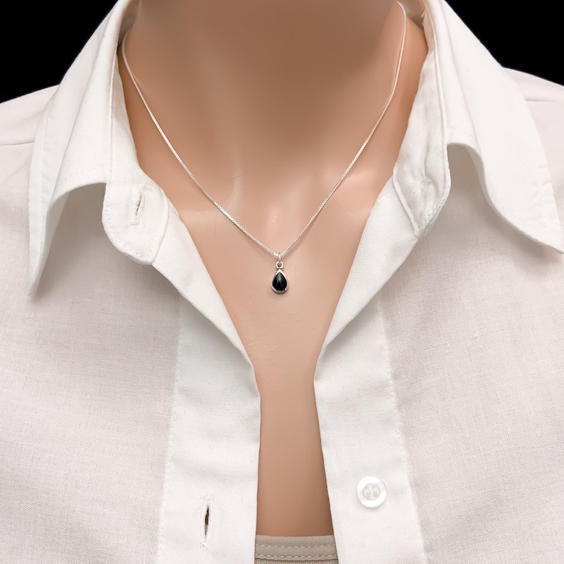 May include: A silver chain necklace with a small black teardrop pendant.