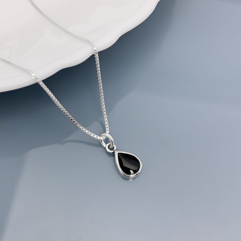 May include: A silver chain necklace with a teardrop-shaped pendant featuring a black gemstone.