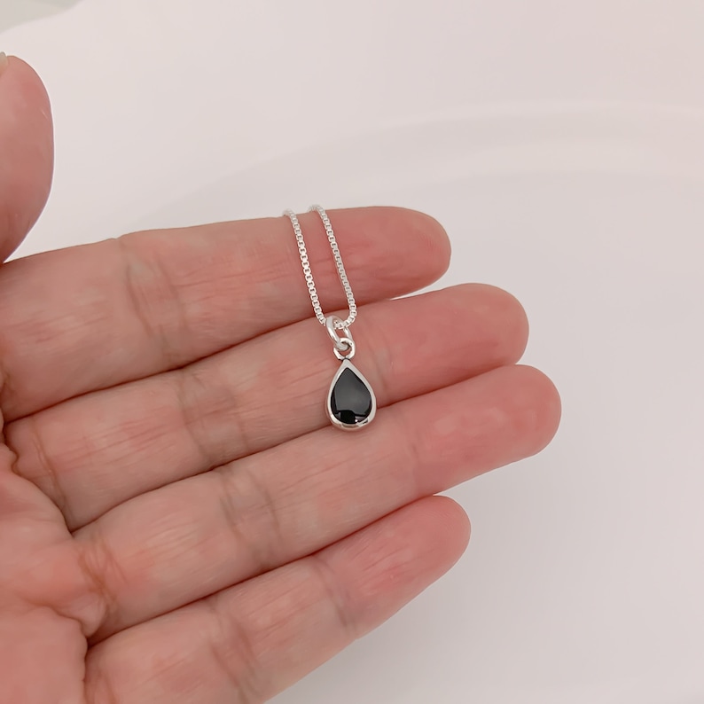 May include: A silver chain necklace with a teardrop-shaped black gemstone pendant.