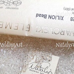 May include: A collection of clear, faceted 4 mm Swarovski XILION beads. The beads are displayed alongside their original white packaging, which features the text SWAROVSKI ELEMENTS, 5328 XILION Bead, 4 mm Crystal (001), and 103557987.