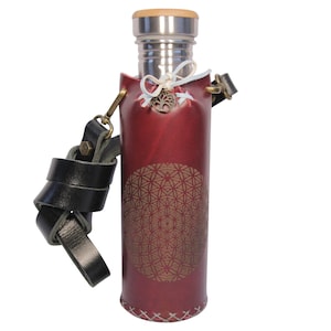 Puede incluir: Un porta-botellas de agua de cuero rojo con una correa negra y una botella de agua de acero inoxidable en el interior. El porta-botellas tiene un diseño geométrico y un amuleto de árbol de la vida.