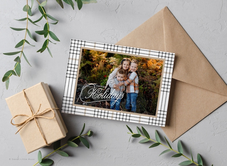 May include: A holiday card with a black and white plaid border. The card features a photo of three children smiling in a forest setting. The text "Happy Holidays" is written in cursive on the card.