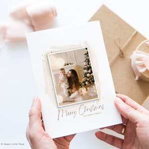Puede incluir: Una tarjeta de Navidad con una foto de una madre y un ni&ntilde;o frente a un &aacute;rbol de Navidad decorado. La tarjeta tiene un fondo de purpurina dorada y el texto "Feliz Navidad La familia Mark".