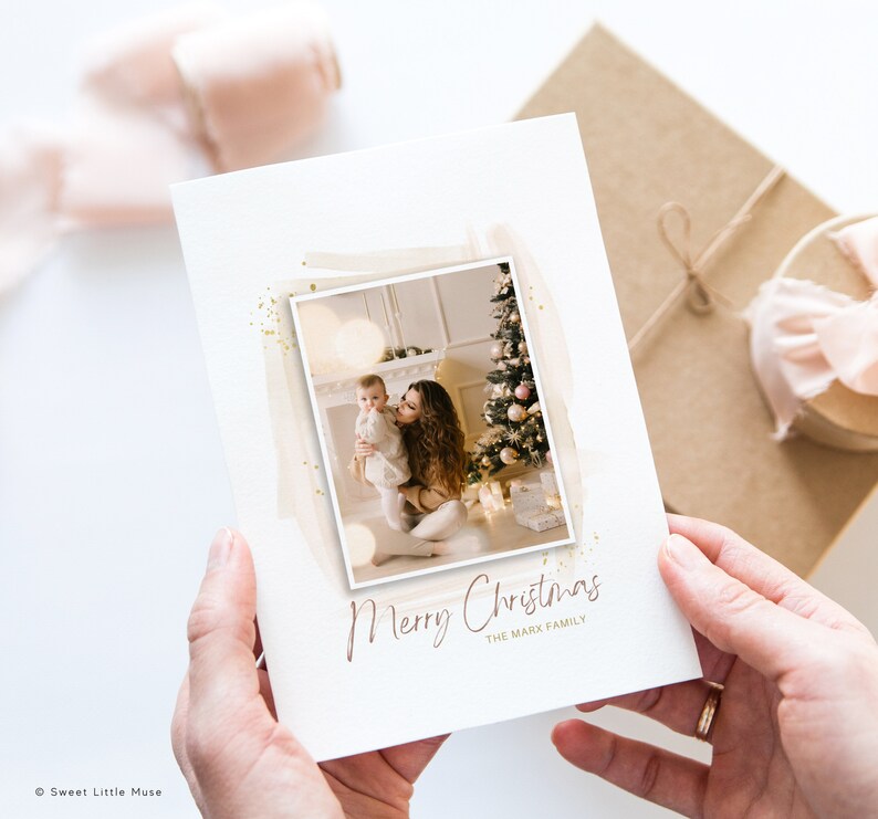 Puede incluir: Una tarjeta de Navidad con una foto de una madre y un ni&ntilde;o frente a un &aacute;rbol de Navidad decorado. La tarjeta tiene un fondo de purpurina dorada y el texto "Feliz Navidad La familia Mark".