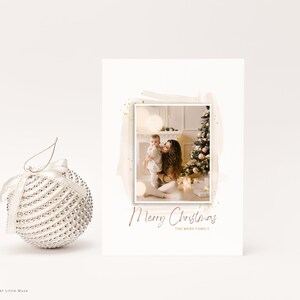 Puede incluir: Una tarjeta de Navidad con una foto de una madre y un ni&ntilde;o frente a un &aacute;rbol de Navidad decorado. La tarjeta tiene un fondo blanco con un dise&ntilde;o de estilo acuarela marr&oacute;n y purpurina dorada. El texto "Feliz Navidad" est&aacute; escrito en cursiva en color marr&oacute;n. El texto "La familia Mark" est&aacute; escrito en una fuente m&aacute;s peque&ntilde;a debajo del saludo.