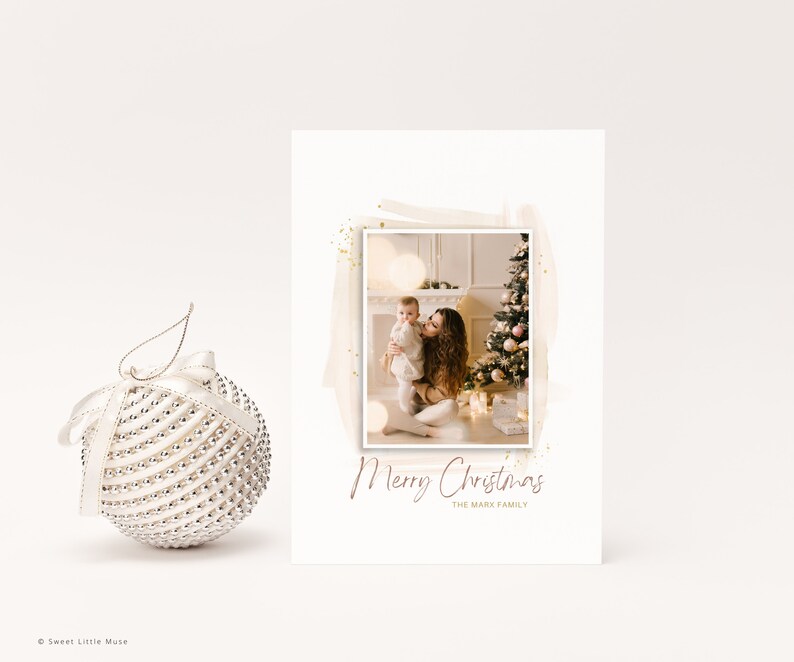 Puede incluir: Una tarjeta de Navidad con una foto de una madre y un ni&ntilde;o frente a un &aacute;rbol de Navidad decorado. La tarjeta tiene un fondo blanco con un dise&ntilde;o de estilo acuarela marr&oacute;n y purpurina dorada. El texto "Feliz Navidad" est&aacute; escrito en cursiva en color marr&oacute;n. El texto "La familia Mark" est&aacute; escrito en una fuente m&aacute;s peque&ntilde;a debajo del saludo.