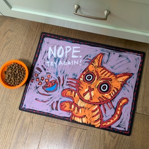 May include: A purple and black cat themed doormat with the text "NOPE. TRY AGAIN!" in white. The cat is orange and has large eyes.