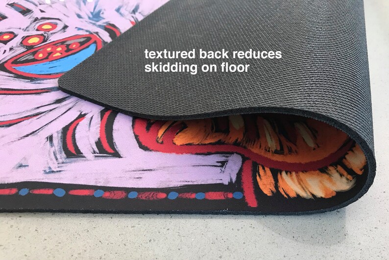 May include: A colorful, abstract design printed on a non-slip yoga mat. The back of the mat is black and textured to prevent slipping on the floor. "textured back reduces skidding on floor" is written on the mat.