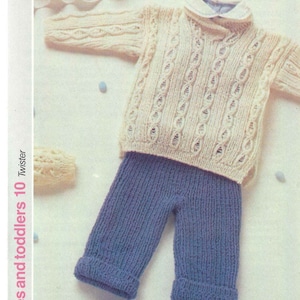 Könnte beinhalten: Ein gestricktes Baby-Pullover- und Hosen-Set. Der Pullover ist cremefarben mit einem Zopfmuster. Die Hose ist blau und hat eine gerippte Strickstruktur.  "Babies and toddlers 10 Twister" ist auf der Seite des Bildes gedruckt.
