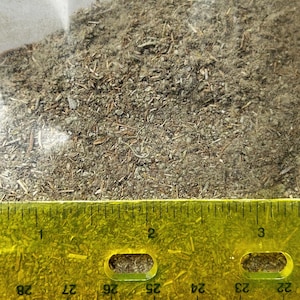 Peut inclure: Gros plan sur un tas d'herbes séchées et de matières végétales, avec une règle jaune en bas. Les herbes sont un mélange de vert, de brun et de gris, avec une variété de textures. La règle indique des mesures en centimètres.