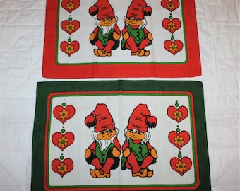 2 Swedish place mats with bright red and green borders, hearts, and a pair of large tomte or elves