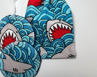 May include: Two reusable makeup remover pads with a blue and white shark print. The pads are in a drawstring bag with the same print.