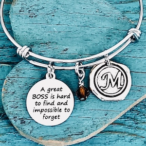 May include: A silver charm bracelet with a charm that reads "A great BOSS is hard to find and impossible to forget". The bracelet also has a charm with the letter "M" and a small brown crystal charm.