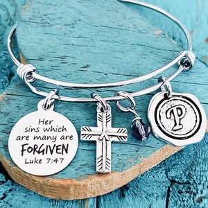 May include: A silver charm bracelet with a cross charm, a charm with the text "Her sins which are many are FORGIVEN Luke 7:47", and a charm with the letter "P".