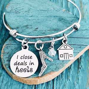 May include: Silver charm bracelet with a charm that says "I close deals in heels". The bracelet also has charms of a high heel shoe, a house, and a crystal.