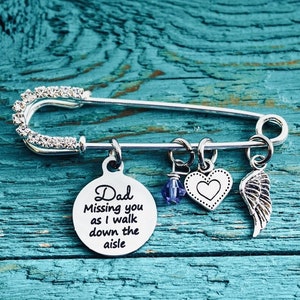 May include: Silver safety pin with charms, including a heart charm and a charm with the text "Dad Missing you as I walk down the aisle".
