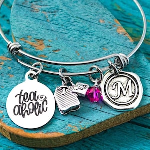 May include: A silver charm bracelet with a heart-shaped charm that says "teaholic" and other charms, including a teacup, a letter "M", and a pink crystal.