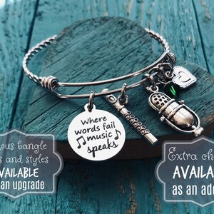 May include: Silver charm bracelet with a microphone, flute, and heart charms. The charm with the microphone has the text "Where words fail music speaks".