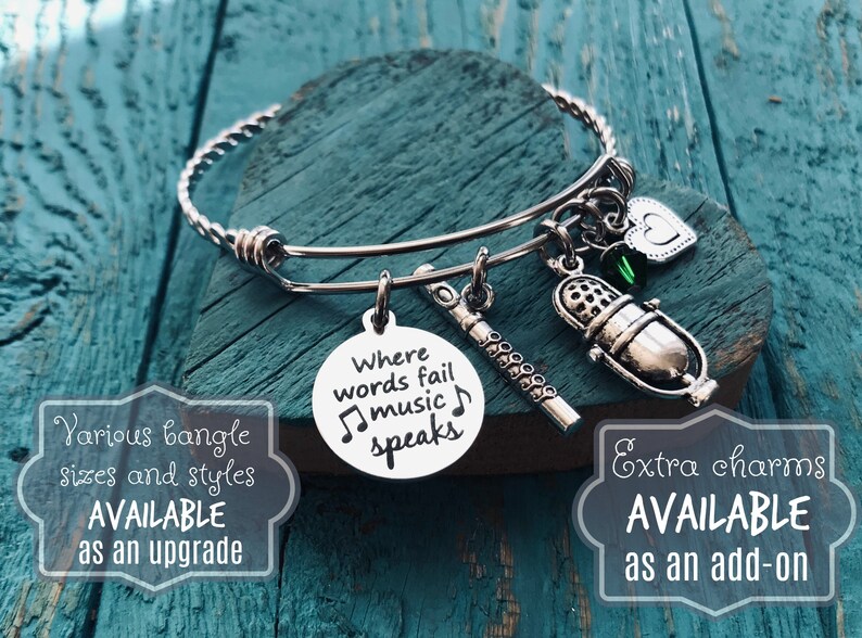 May include: Silver charm bracelet with a microphone, flute, and heart charms. The charm with the microphone has the text "Where words fail music speaks".