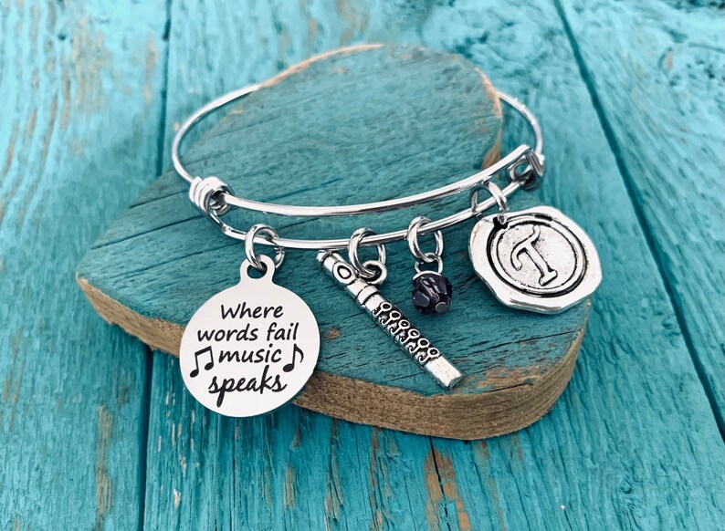 May include: A silver charm bracelet with a charm that says "Where words fail music speaks" and a charm that looks like a flute. The bracelet also has a charm with the letter "T" and a black bead.