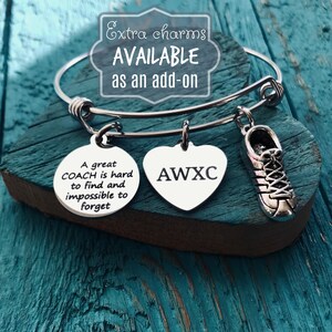 May include: A silver charm bracelet with three charms: a round charm with the text "A great COACH is hard to find and impossible to forget", a heart charm with the text "AWXC", and a shoe charm.