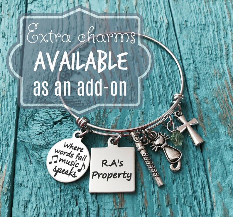 May include: A silver charm bracelet with various charms, including a music note charm with the text "Where words fail music speaks", a square charm with the text "R.A's Property", a cat charm, a cross charm, and a green crystal charm.
