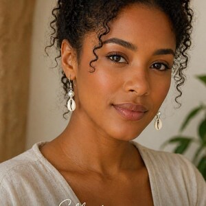 May include: A woman wearing shell earrings with a pearl accent. The earrings are hanging from silver hooks. The image includes the text "Effortless Everyday Elegance" and the logo for KHEPERA Adornments LLC.