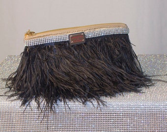 May include: A black feather clutch with a gold zipper and a rhinestone trim. The clutch has a small gold label with the text "Remarkable" on it.