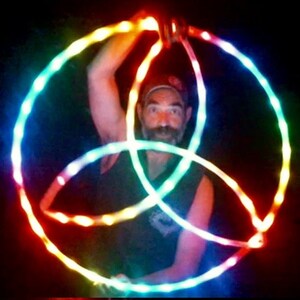 May include: A person is holding three glowing LED hoops in a rainbow pattern. The hoops are intertwined and create a circular design.