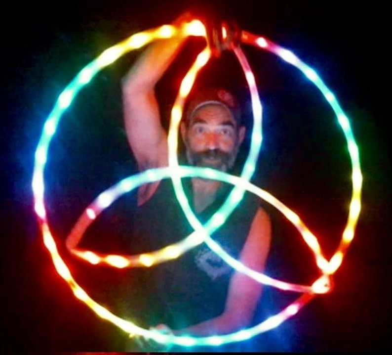 May include: A person is holding three glowing LED hoops in a rainbow pattern. The hoops are intertwined and create a circular design.