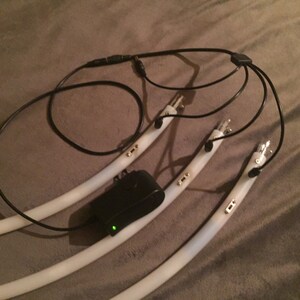 May include: Three white flexible LED light strips with black wires and a black power adapter. The light strips have gold connectors and are connected to a black Y-shaped connector.