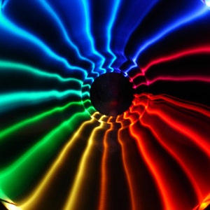 May include: A colorful abstract image with a swirling pattern of blue, green, yellow, orange, and red light. The light appears to be emanating from a central point and radiating outwards.