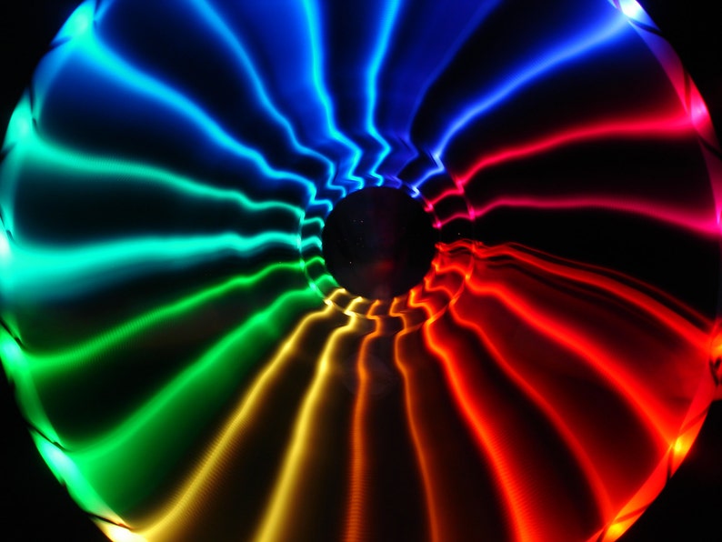 May include: A colorful abstract image with a swirling pattern of blue, green, yellow, orange, and red light. The light appears to be emanating from a central point and radiating outwards.