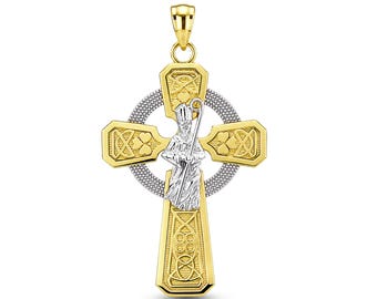 Może przedstawiać: Dwukolorowy wisiorek w kształcie krzyża celtyckiego ze złota i srebra, przedstawiający postać biskupa trzymającego pastorał. Ramiona krzyża ozdobione są misternymi splotami i motywami koniczyny, a okrągły pierścień ma teksturowane wykończenie.