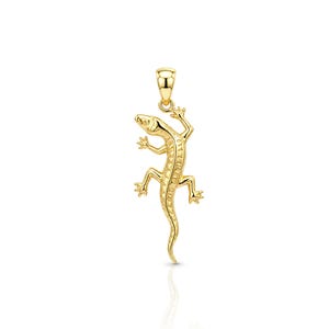 May include: A polished gold pendant shaped like a lizard, featuring a textured back and a small loop at the top for attachment. The lizard is depicted in a climbing position with four legs extended and a long, curved tail pointing downwards.