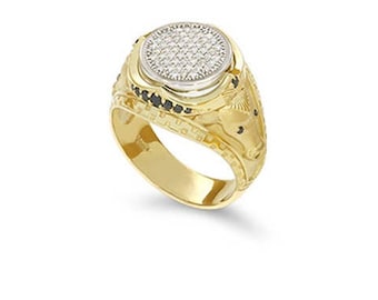 May include: A gold ring with a round, diamond-studded center. The ring has a two-tone design, with a silver-colored border around the diamonds. Black stones are set on the sides of the ring. The band is engraved with a detailed pattern.