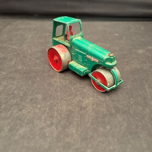May include: A green toy road roller with red wheels and a red figure in the driver's seat. The toy has the text "WILLSHIRE  ROAD  ROLLER" on the side.