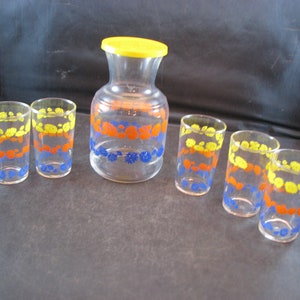 Puede incluir: Un juego de siete recipientes de vidrio para bebidas con una tapa amarilla. Los recipientes tienen un patrón floral en azul, amarillo y naranja.