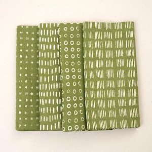 May include: Four folded green cloth napkins with white patterns. The patterns include vertical lines, dashes, and circles. The napkins are arranged side by side, showcasing the variety of designs. These napkins are suitable for kitchen or dining room use.