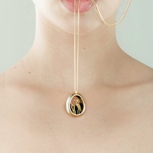 May include: A gold chain necklace with a pendant featuring a detailed silhouette of a bird in a gold oval frame.