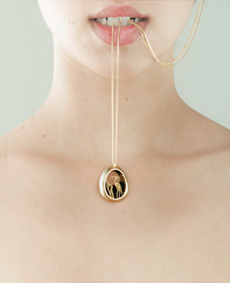 May include: A gold chain necklace with a pendant featuring a detailed silhouette of a bird in a gold oval frame.