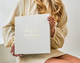 May include: A white photo album with gold lettering that reads "Marlene & Alexander 08.15.2024".
