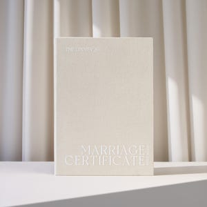May include: A cream-coloured rectangular marriage certificate holder with a textured fabric cover. The text THE LINNEY'S is printed at the top, and MARRIAGE CERTIFICATE 09.19.2026 is printed in large white capital letters at the bottom.