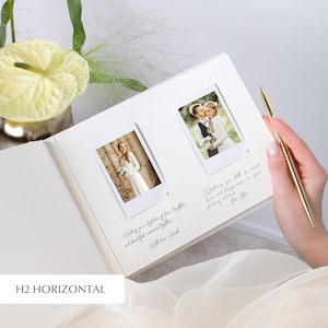 Open ivory wedding guest book held on the bride’s lap, two Instax/Polaroid prints mounted side‑by‑side in white photo corners, dotted lines with tiny heart icons for guest messages below each image; bride holding a gold pen, pale green flowers and airy greenery in the background.