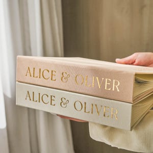 Stacked wedding guest books in sand and ivory colors with matching gold foil names ‘Alice & Oliver’, premium slip-in albums for instant photos