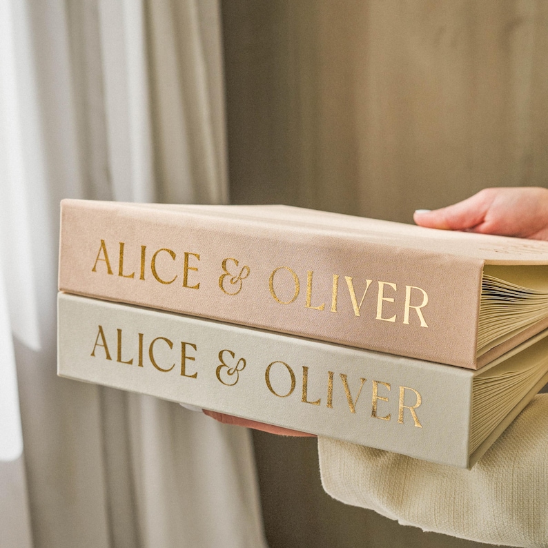 Stacked wedding guest books in sand and ivory colors with matching gold foil names ‘Alice & Oliver’, premium slip-in albums for instant photos