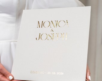 May include: White wedding guest book with gold foil lettering. The names "Monica & Joseph" are printed on the front cover, along with the date "Colorado, 29.08.2024".