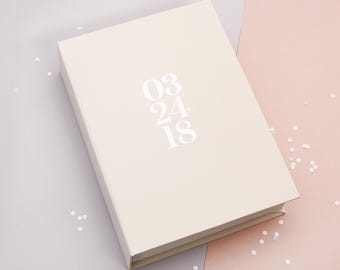 May include: A white box with the date "03 24 18" printed on it. The box is sitting on a light pink and gray surface with white confetti.
